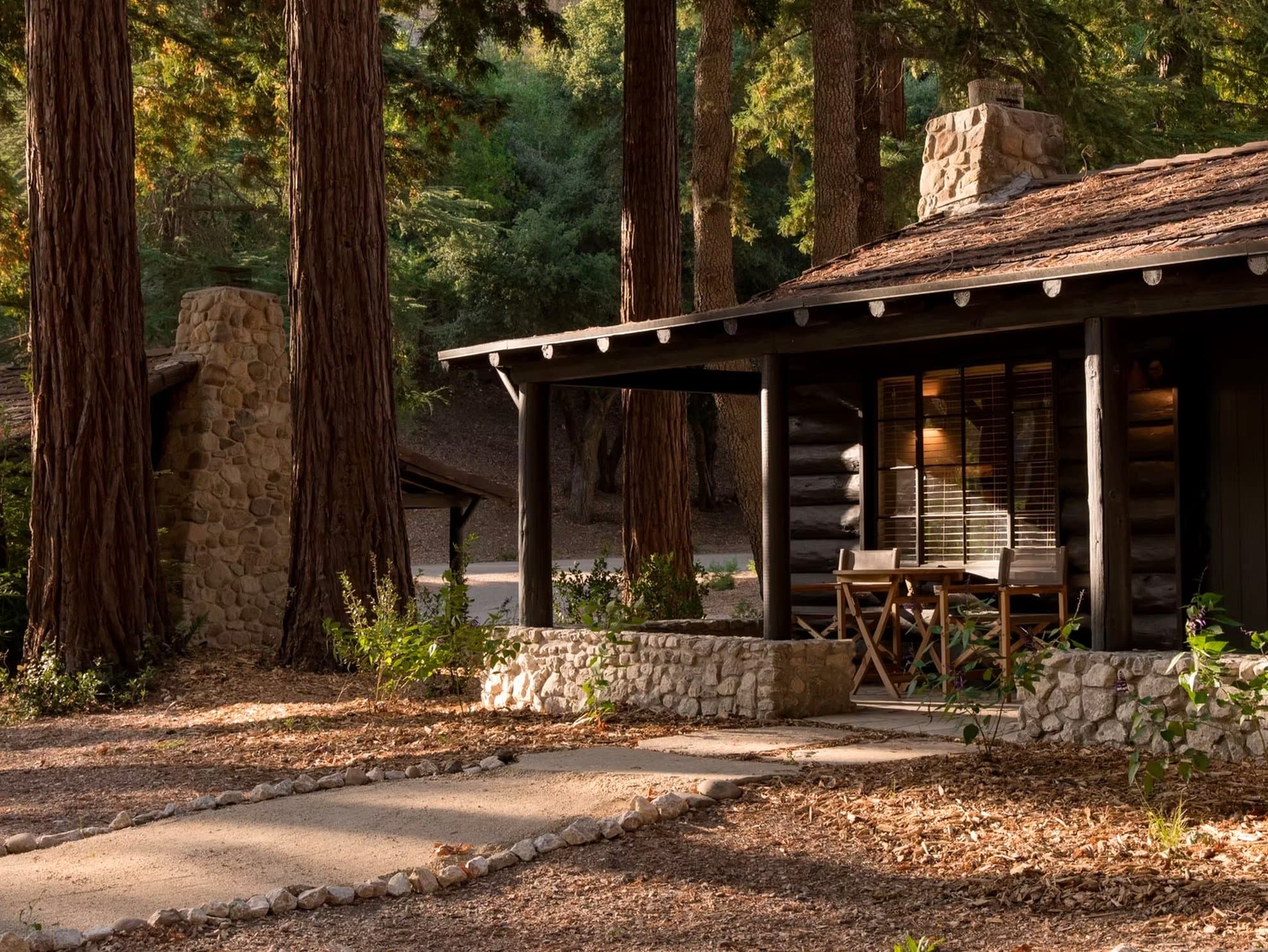 A log cabin with a stone chimney under the redwoods